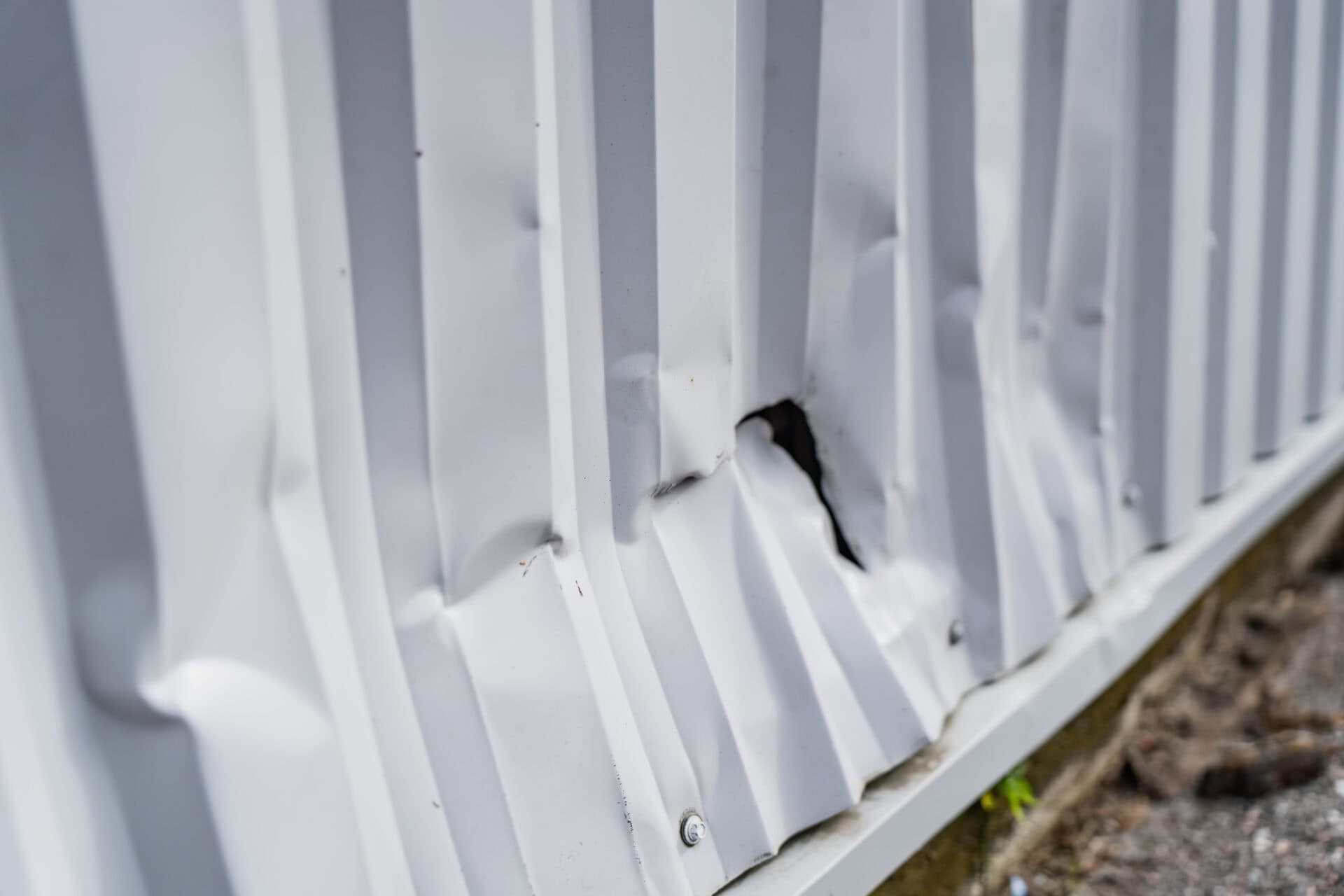 Bent corrugated metal cladding panel displaying a major impact indentation and rupture hole from a workplace collision or structural accident