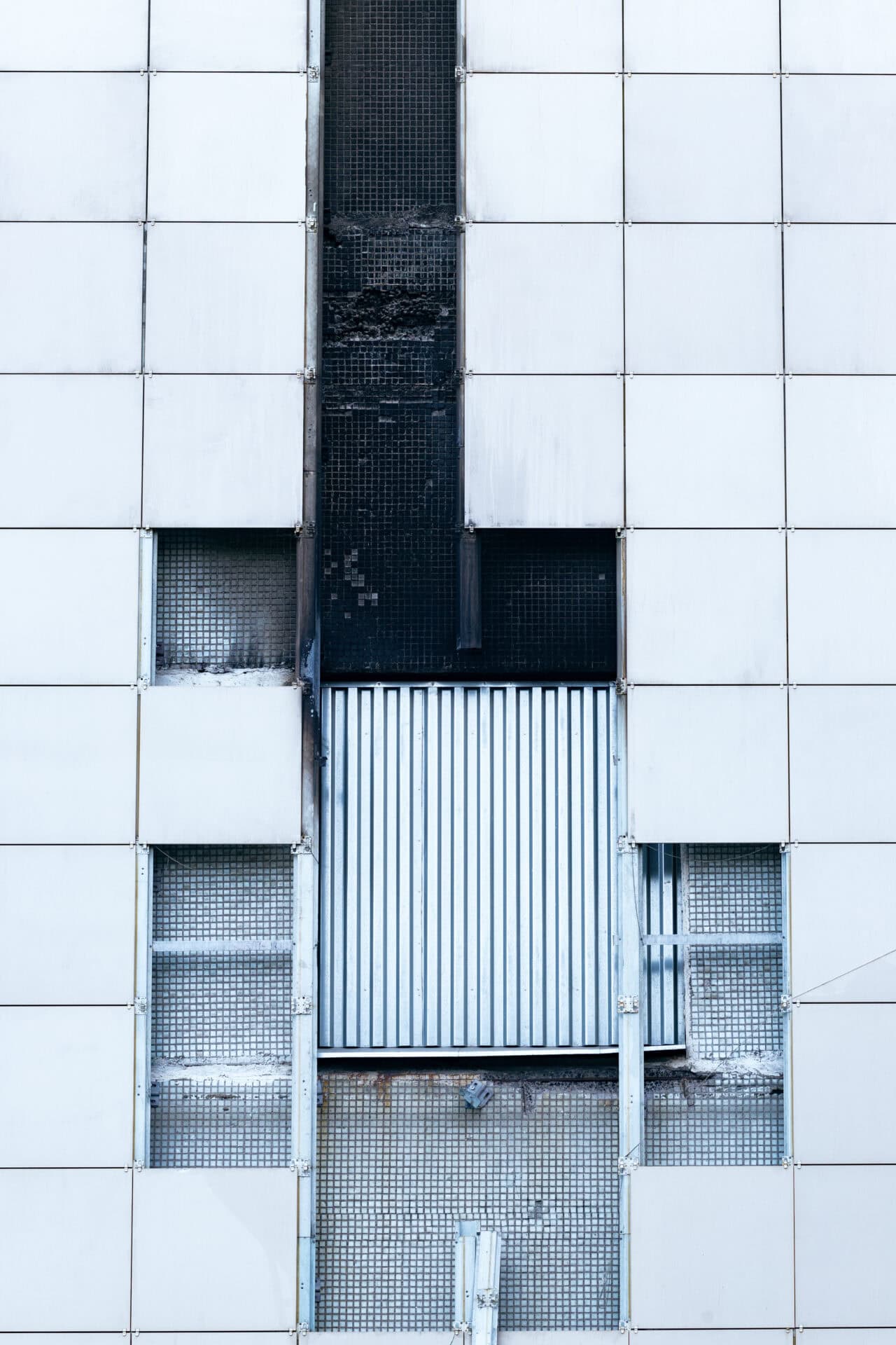 Broken, badly fixed wall of an industrial building. Fallen off cladding tiles of the outer skin, the inner parts of the wall are visible. Metal, concrete.